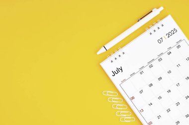 Temmuz 2025, 2025 yılı için aylık masa takvimi ve sarı arkaplanlı ataçlı kalem. Kopyalama alanı olan konum.