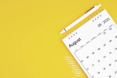 Ağustos 2025, 2025 yılı için aylık masa takvimi ve sarı arkaplanlı ataçlı kalem. Kopyalama alanı olan konum.