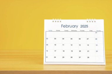 Şubat 2025, 2025 tarihli aylık masa takvimi sarı arka planlı ahşap masa üzerinde..