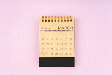 Arka plan olarak kabartmalı çiçek deseni üzerine Mart 2025 için kahverengi kağıt masa takvimi.