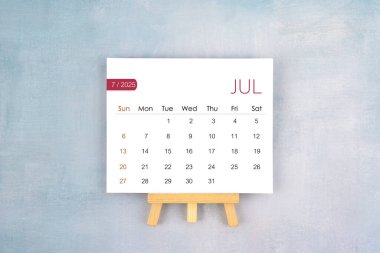 July 2025 calendar page with wooden easel, Flat lay.