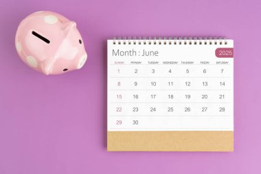 Haziran 2025. Masa takvimi ve mor arka planda pembe kumbara..