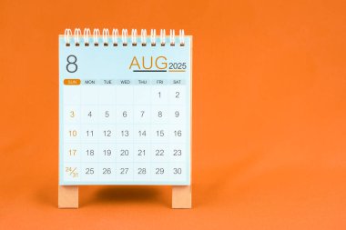 Ağustos 2025 Turuncu renkli tekstil arkaplanı üzerinde duran masa başı takvimi.