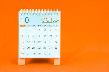 Ekim 2025, masa takvimi turuncu renkli tekstil arkaplanı üzerine duruyor.