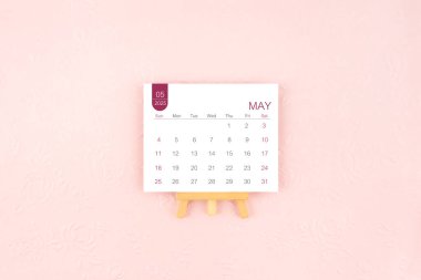 Mayıs 2025 takvim sayfası pembe arka planda ahşap sehpa ile.