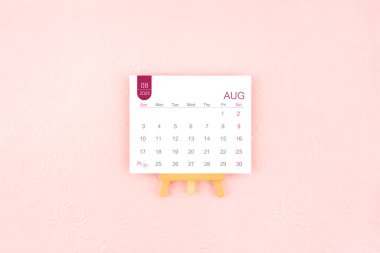 Pembe arka planda ahşap sehpası olan Ağustos 2025 takvim sayfası.