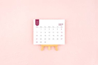 Eylül 2025 takvim sayfası Pembe arka planda ahşap sehpa.