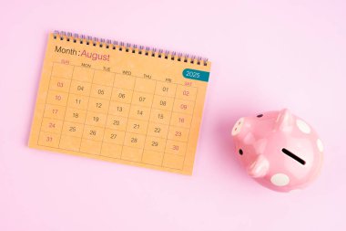 Ağustos 2025 için kahverengi masa takvimi ve pembe domuz kumbarası.