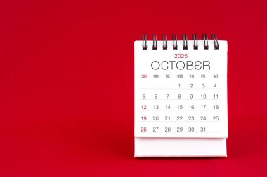 Ekim 2025 için kırmızı arkaplan üzerine beyaz masa takvimi.