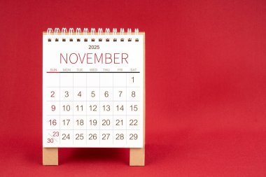 Kırmızı arkaplanda Kasım 2025 için boş masa takvimi.