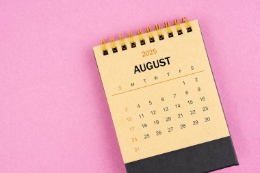 Pembe arka planda Ağustos 2025 için kahverengi masa takvimi.