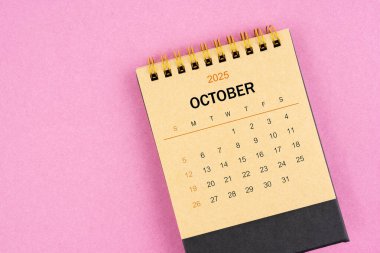 Pembe arka planda Ekim 2025 için kahverengi masa takvimi.
