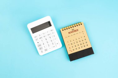 Mavi arkaplan üzerinde Kasım 2025 kahverengi kakülatör ve beyaz hesap makinesi.