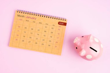 Ocak 2026 için kahverengi masa takvimi ve pembe domuz kumbarası.
