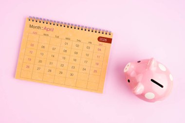Nisan 2026 için kahverengi masa takvimi ve pembe kumbara.