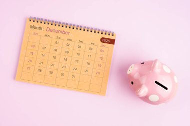 Aralık 2026 için kahverengi masa takvimi ve pembe kumbara.