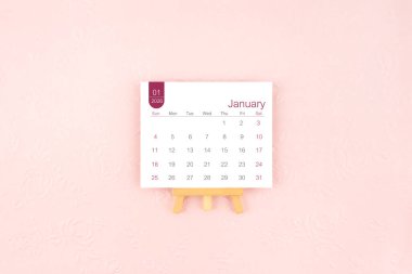 Ocak 2026 takvim sayfası Pembe arka planda ahşap sehpa.