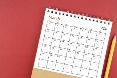 Kırmızı zemin üzerinde Mart 2026 masa takvimi ve kalem.