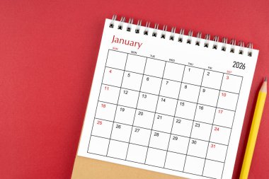 Kırmızı arkaplanda Ocak 2026 masa takvimi ve kalem.