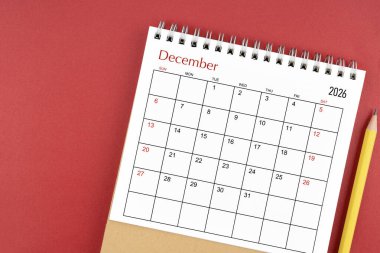 Aralık 2026 Kırmızı zemin üzerinde masa takvimi ve kalem.