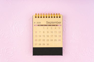 Arka plan olarak kabartmalı çiçek deseni üzerine Eylül 2026 için kahverengi kağıt masa takvimi.