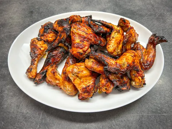 Golden grilled marinated chicken wings and thighs on white plate - detail from home kitchen