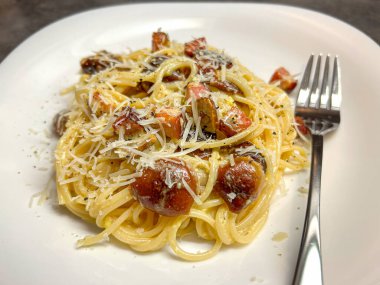 Pastırma, yumurta, mantar ve beyaz tabakta parmesan peyniri ile spagetti ala Carbonara. Ev mutfağının ayrıntıları.