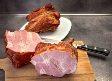 Büyük füme domuz parçaları tabakta ve ahşap mutfak kesme tahtasıyla ev mutfağından ateşlenmiş.