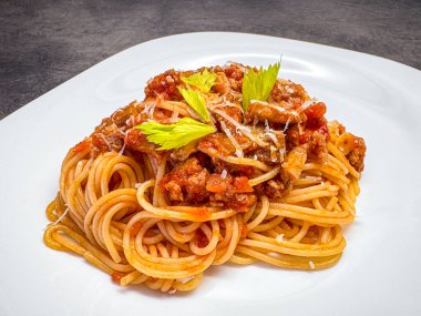 Beyaz tabakta yeşil kereviz yapraklarıyla süslenmiş spagetti üzerine domates eti karışımı.