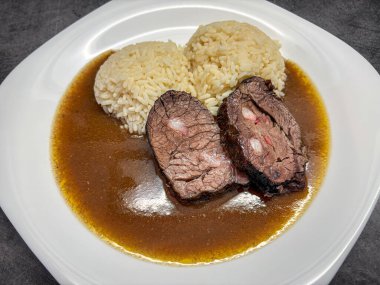 Domuz pastırması, kahverengi sos ve pirinçli biftek dilimli beyaz tabak yakın çekim.