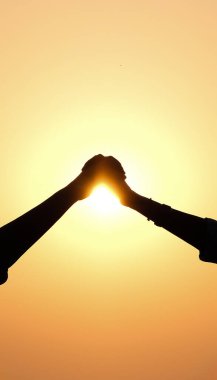 Gün batımında gökyüzünde el ele tutuşan aşkın silueti.