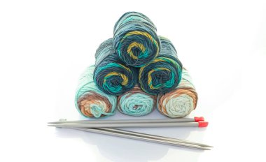 Beyaz arka planda yün topları ve örgü iğneleri var.