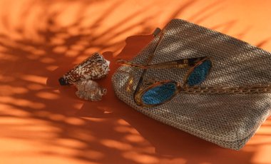 Yaz konsepti, hasır çanta, güneş gözlüğü ve gölgede deniz kabukları.