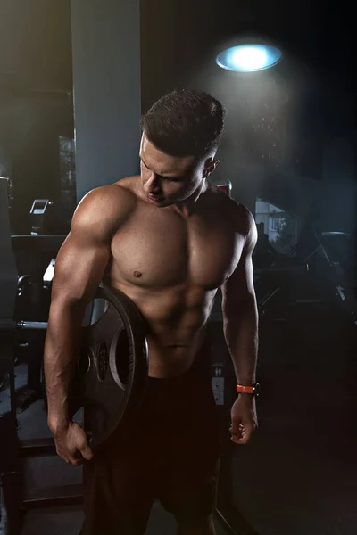Muscular guy posing in the gym, creative photo, with a watch on his hands and holding a heavy weight, looks away, beautiful body, physique, relief, sexy guy, young.Handsome strong athletic men pumping up muscles workout bodybuilding