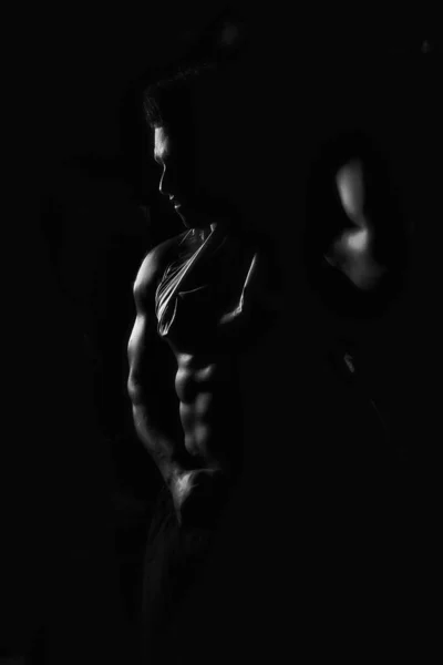 The athlete shows his body and abs, creative photo, black and white photo, contours, muscles stand out, beautiful body, physique, relief, sexy guy, young.