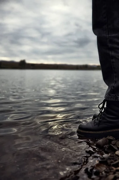 an abandoned teenager a man stands by the water, looks and reflects on the hard life of shoes in the water. High quality photo