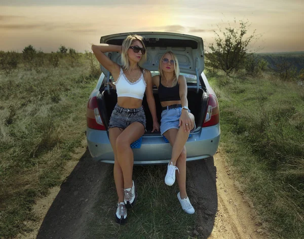 an accident on the road, a car broke down, two beautiful girl models are hitchhiking a car. Showing the thumb up. Problem with the car. Friends waiting for service. In the countryside . High quality