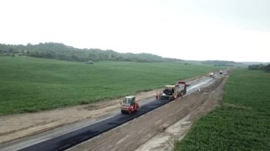 Asphalt paver, roller and truck on the road repair site during asphalting timelapse. Road construction equipment. Workers repairing. Trucks are working near the highway. Cars moving on the road. New