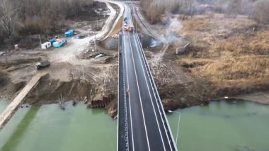 Aerial view of a road bridge under construction. road and bridge under construction. view from the sky. Modernization of the structure across the river. Black long road. Asphalt. Workers on a large