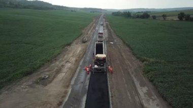 Asphalt paver, roller and truck on the road repair site during asphalting timelapse. Road construction equipment. Workers repairing. Trucks are working near the highway. Cars moving on the road. New