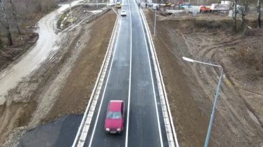 İnşaat halindeki bir yol köprüsünün havadan görüntüsü. Yol ve köprü yapım aşamasında. Gökyüzünden manzara. Nehrin karşısındaki yapının modernizasyonu. Siyah uzun yol. Asfalt. Büyük çaplı işçiler.