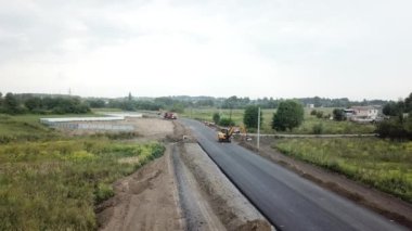 Asphalt paver, roller and truck on the road repair site during asphalting timelapse. Road construction equipment. Workers repairing. Trucks are working near the highway. Cars moving on the road. New