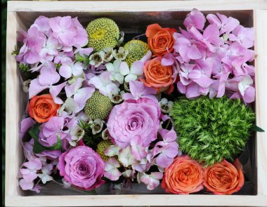 Ahşap kutunun içindeki çiçeklerin en üst görüntüsü mor güller ve renkli arka plan