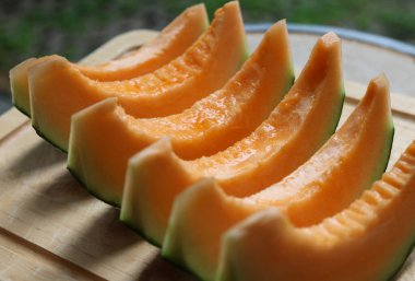 Tatlı kavun, içi turuncu, dilimlenmiş tahta kesme tahtasına konmuş.