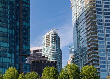 Tall buildings line the skyline, showcasing modern architecture and glass facades. Lush trees provide a refreshing contrast against the urban backdrop on a sunny day.