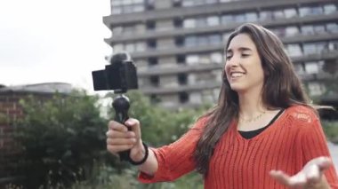 Hırslı genç bir kadın, gaddar mimarinin önünde vlogluk yapıyor.