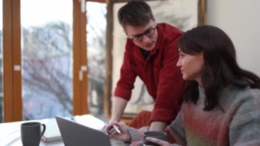 İki meslektaş, bir erkek ve bir kadın, parlak bir ofiste dizüstü bilgisayarda birlikte çalışıyorlar, takım çalışması ve işbirliği gösteriyorlar.