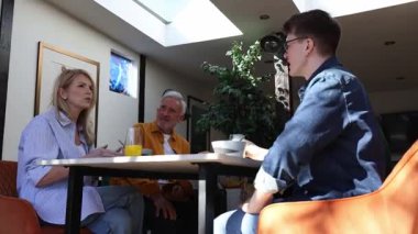 Aile kahvaltı yapıyor ve modern evlerinde konuşuyor.