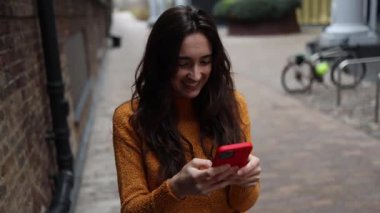 Mutlu kadın akıllı telefon kullanıyor ve ara sokakta gülümsüyor.