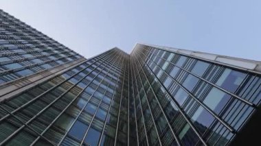 Açık mavi gökyüzüne doğru yükselen modern bir gökdelenin cam cephesi